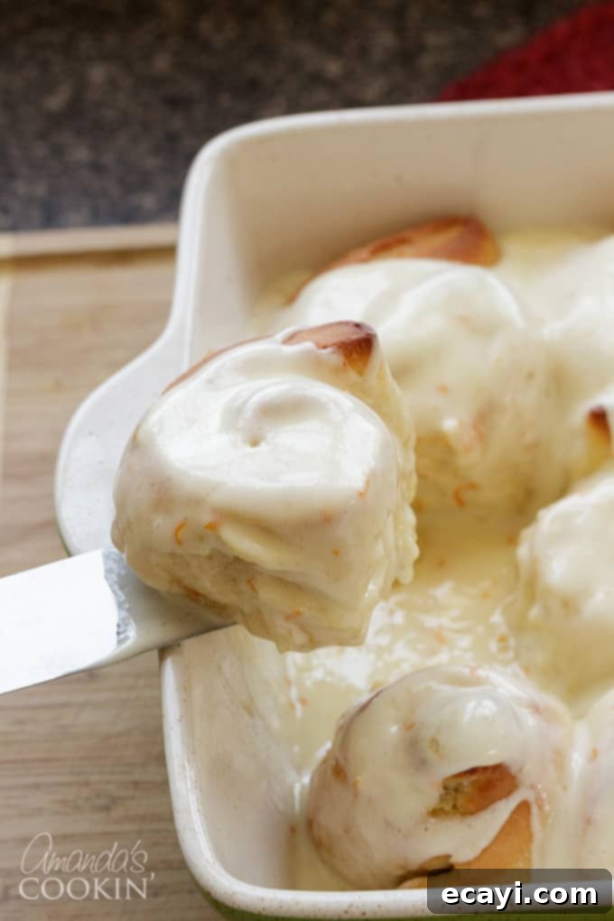 You'll love these orange rolls just as much as homemade cinnamon rolls. This quick orange rolls recipe is ideal for those who prefer homemade over canned. #orangerolls #cinnamonrolls #breakfastrolls #orange #creamcheese #creamcheesefrosting #sweetrolls #orangerollsrecipe #breakfast #sweetrollrecipe taking orange roll out of pan