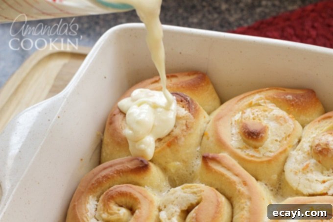 You'll love these orange rolls just as much as homemade cinnamon rolls. This quick orange rolls recipe is ideal for those who prefer homemade over canned. #orangerolls #cinnamonrolls #breakfastrolls #orange #creamcheese #creamcheesefrosting #sweetrolls #orangerollsrecipe #breakfast #sweetrollrecipe adding frosting to orange rolls