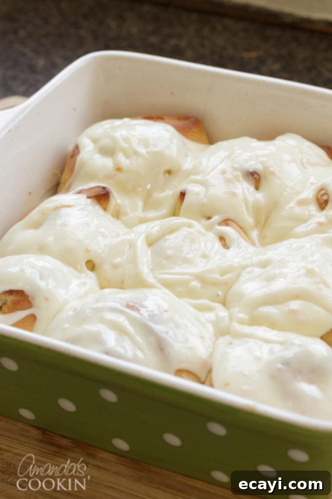 You'll love these orange rolls just as much as homemade cinnamon rolls. This quick orange rolls recipe is ideal for those who prefer homemade over canned. #orangerolls #cinnamonrolls #breakfastrolls #orange #creamcheese #creamcheesefrosting #sweetrolls #orangerollsrecipe #breakfast #sweetrollrecipe frosted orange rolls in pan