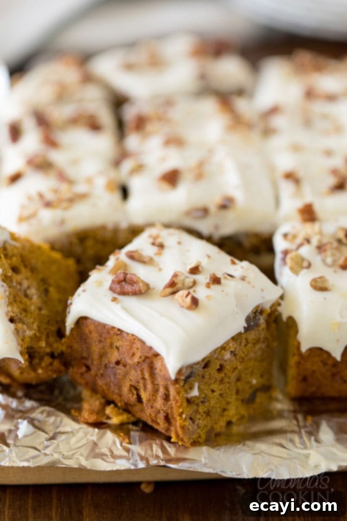 Delicious Fall Spiced Pumpkin Cake with White Chocolate Cream Cheese Frosting and Pecans Frosted pumpkin cake squares on a festive foil with autumn leaves