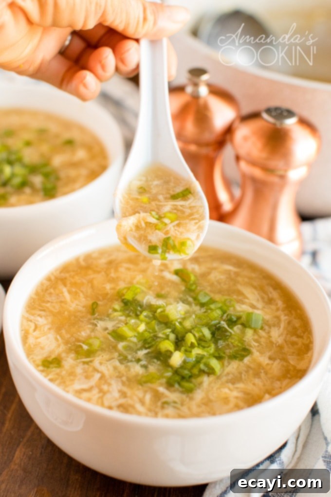 Enjoying a spoon of freshly made Egg Drop Soup – a simple, delicious, and quick Chinese appetizer. hand holding a spoon of delicate egg drop soup with green onions, showcasing the silky egg texture