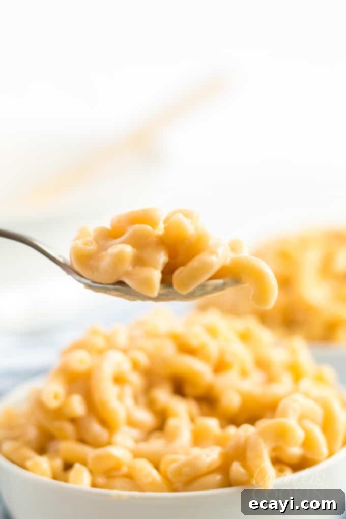 My stovetop mac and cheese recipe is easy to make, uses a homemade cheese sauce, and is perfectly creamy. Make this mac and cheese today! #macaroni #macandcheese #cheese #sides #dinnersides #lunch #pasta A spoonful of creamy homemade stovetop mac and cheese being lifted from the bowl, showcasing its rich texture.