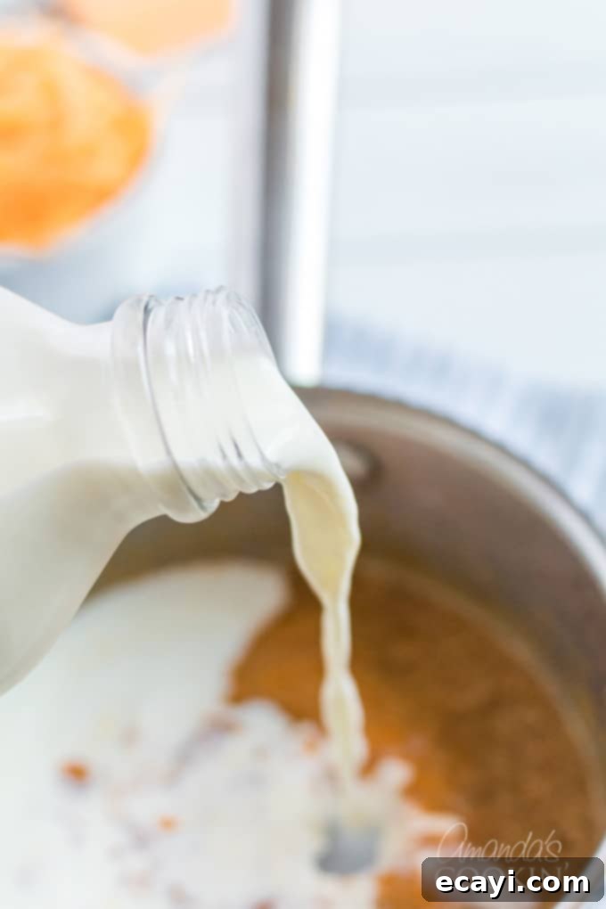 My stovetop mac and cheese recipe is easy to make, uses a homemade cheese sauce, and is perfectly creamy. Make this mac and cheese today! #macaroni #macandcheese #cheese #sides #dinnersides #lunch #pasta Pouring fresh milk into a saucepan, preparing to create the creamy cheese sauce for homemade mac and cheese.