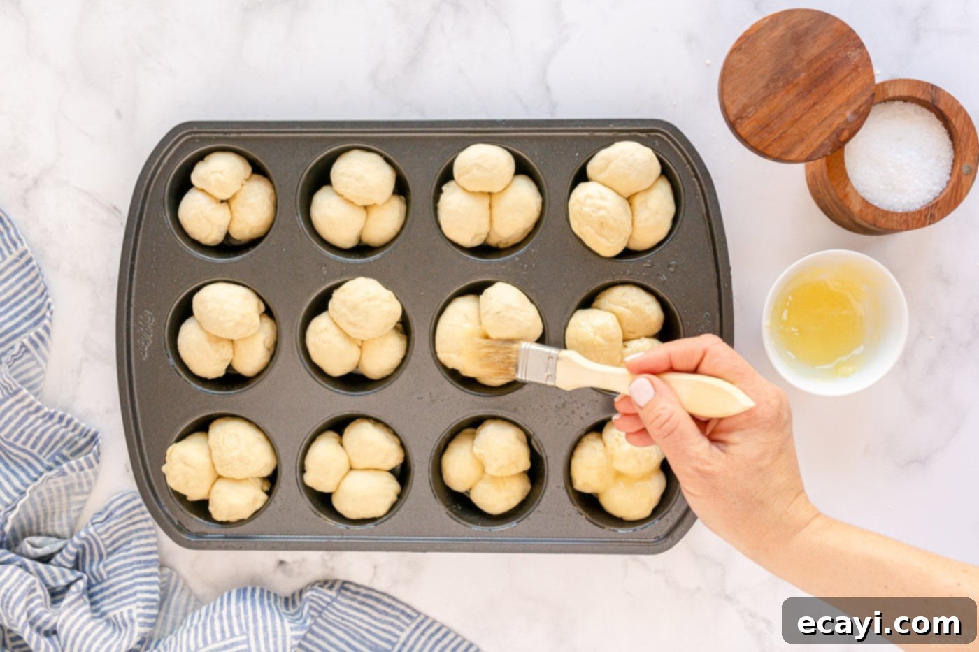 Irresistible Tear-and-Share Dinner Buns 10 Brushing melted butter over the formed dough balls in a muffin pan.
