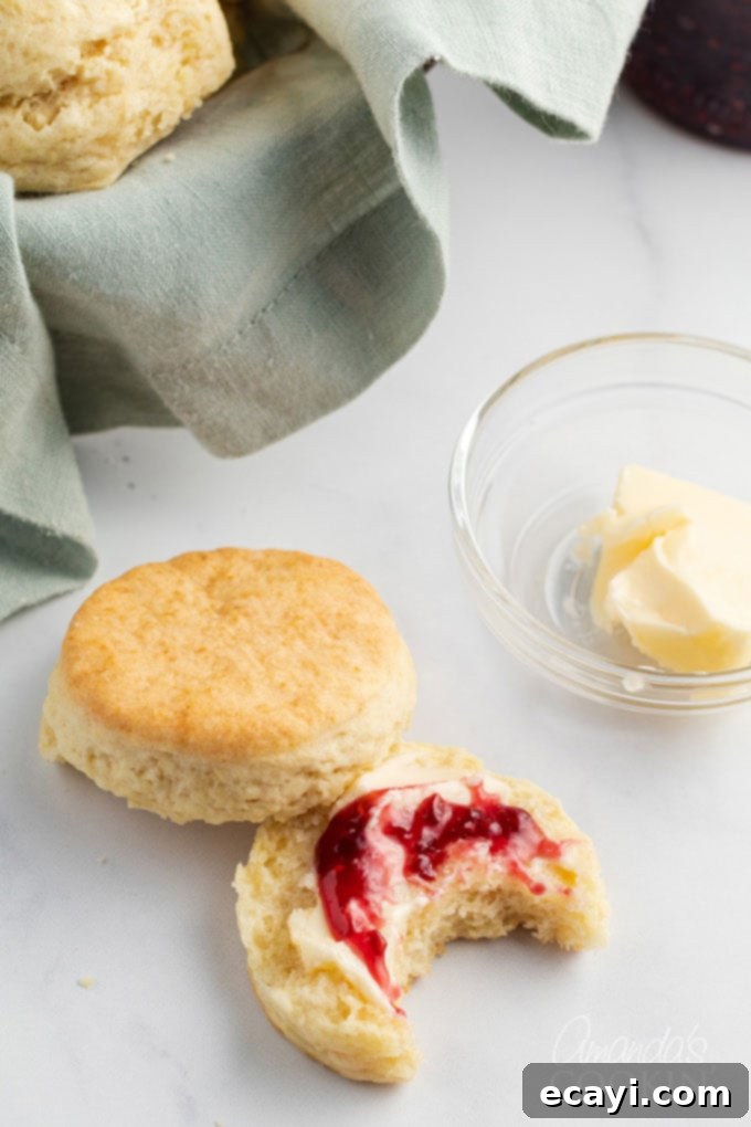 This recipe for flaky homemade biscuits only has 5 ingredients and comes together quickly, getting them on the table in about half an hour. A freshly baked, golden-brown biscuit split open and generously topped with vibrant red berry jam, inviting a delightful bite.