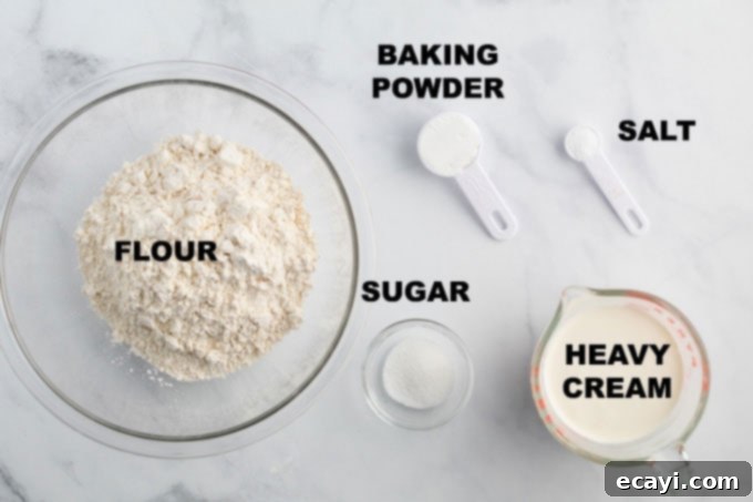 Golden Fluffy Biscuits 2 A flat lay photograph showcasing the five simple ingredients required for homemade biscuits: flour, baking powder, sugar, salt, and a pitcher of heavy cream.