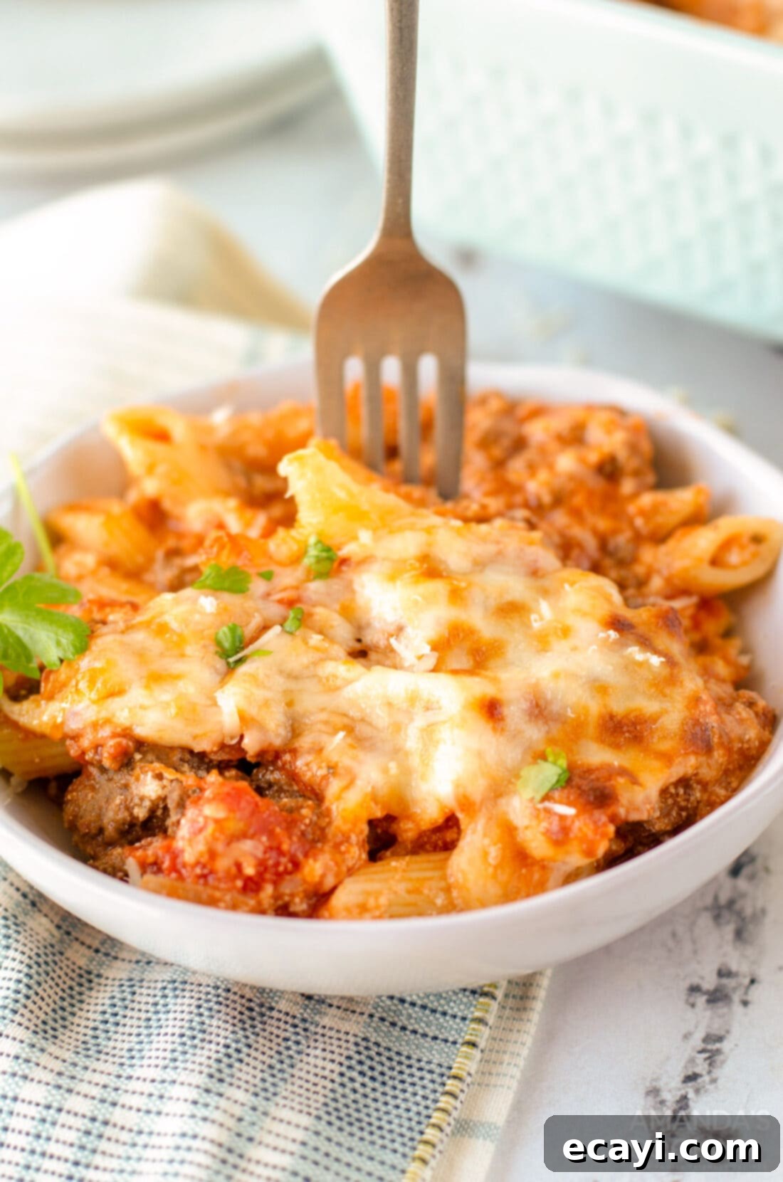 Ultimate Cheesy Ziti Bake 5 A fork piercing into a delicious portion of baked ziti in a bowl, showcasing the melted cheese and hearty sauce