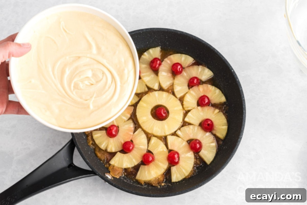 Golden Skillet Pineapple Flip 9 pouring cake batter into a cast iron skillet over pineapple and cherries