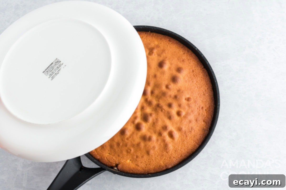 Golden Skillet Pineapple Flip 11 placing a flat plate over the top of a cast iron skillet containing the baked cake, preparing to invert it