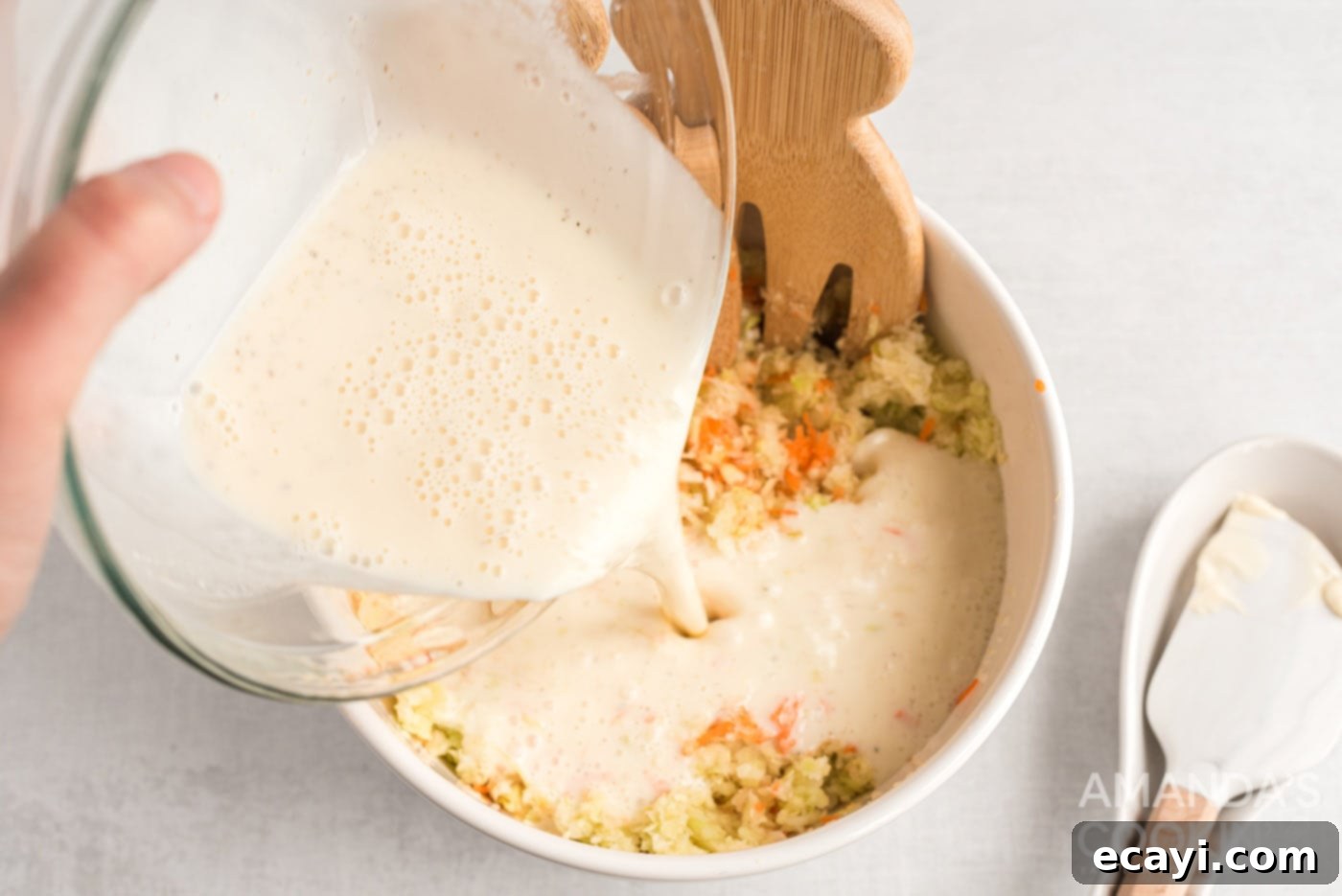 The Ultimate KFC Coleslaw Recipe 5 Pouring the creamy dressing over the chopped cabbage, carrots, and onion for KFC coleslaw.