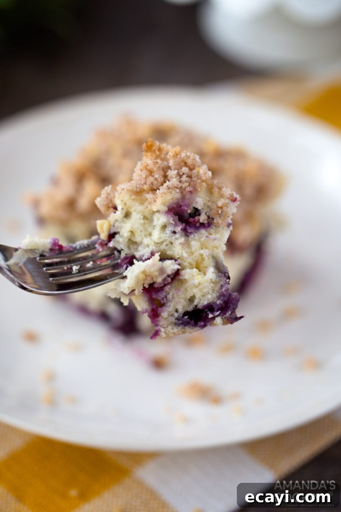 Enjoying a Bite of Blueberry Streusel Cake A fork taking a bite out of a warm slice of blueberry breakfast cake, showing its moist texture.