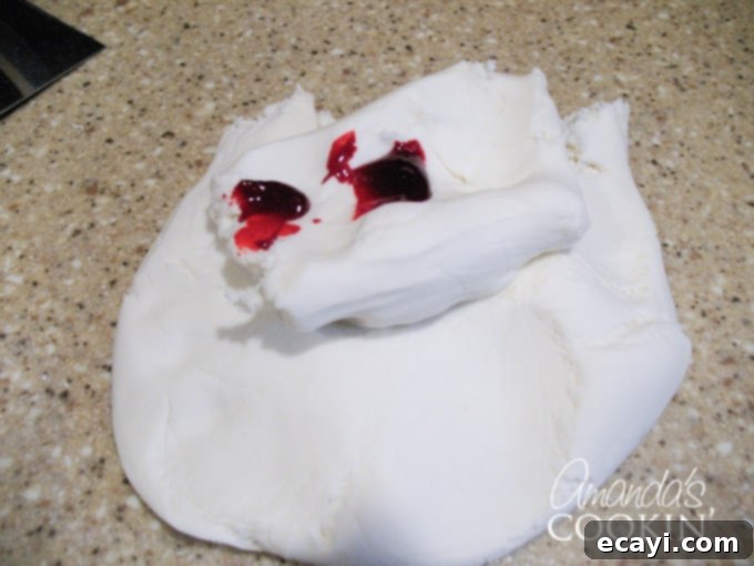 Spiderman Cake Magic: Homemade Marshmallow Fondant 4 A photo of white marshmallow fondant with red gel food coloring on top, ready to be kneaded and colored.