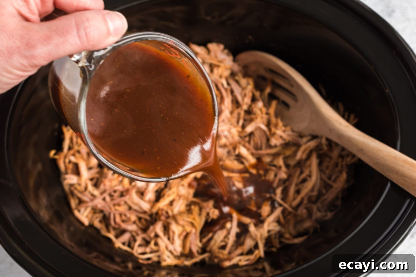 Fall-Apart Tender Slow Cooker Pulled Pork 12 pouring sauce over pulled pork