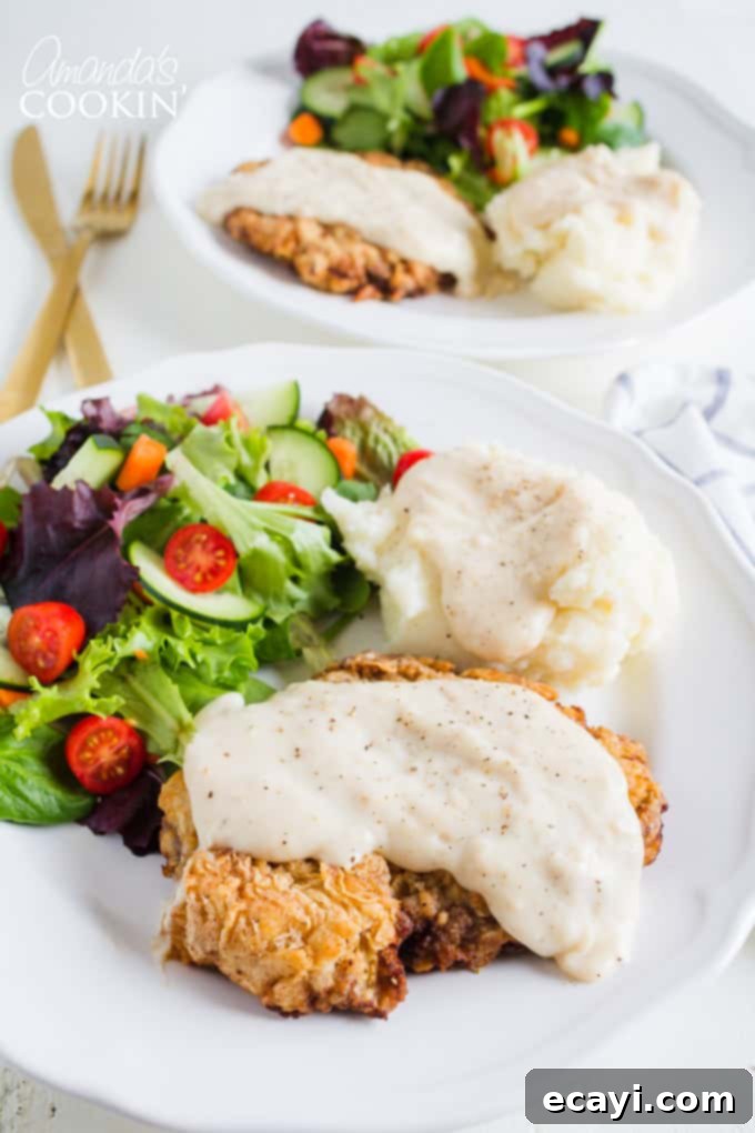 Classic Chicken Fried Steak with homemade gravy, a perfect comfort food dinner with crispy beef, mashed potatoes, and a fresh side salad. chicken fried steak with salad and potatoes on a plate, topped with creamy white gravy