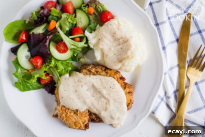 Close-up of a perfectly fried chicken fried steak with creamy gravy and a fresh side salad. chicken fried steak with gravy and side salad