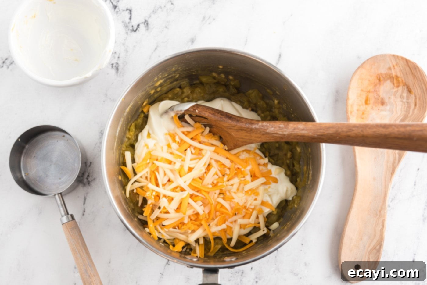 Zesty Chicken Chile Enchiladas 12 Sour cream and shredded cheese being added to the pan with green chiles, creating a creamy sauce.