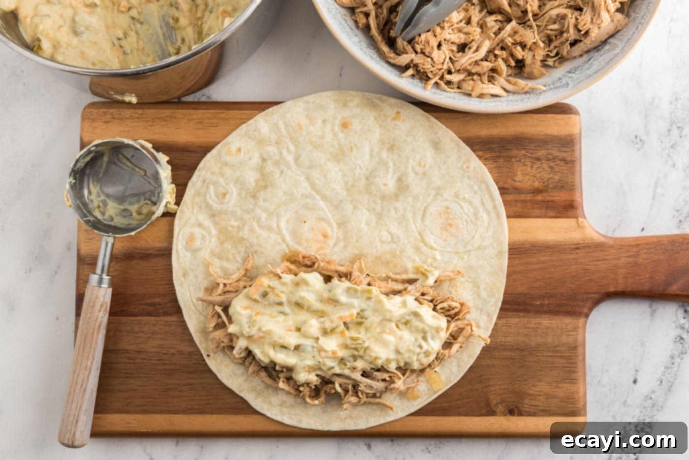 Zesty Chicken Chile Enchiladas 15 Creamy green chile sauce being spread on top of shredded chicken on a tortilla before rolling.