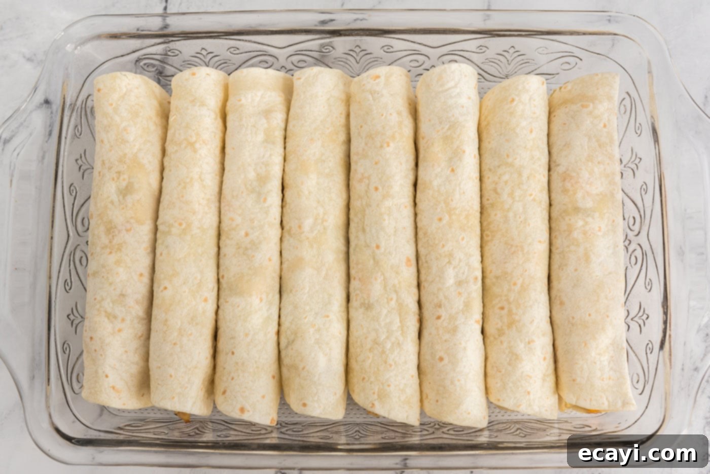 Zesty Chicken Chile Enchiladas 16 Neatly rolled enchiladas arranged seam-side down in a baking dish, ready for the oven.
