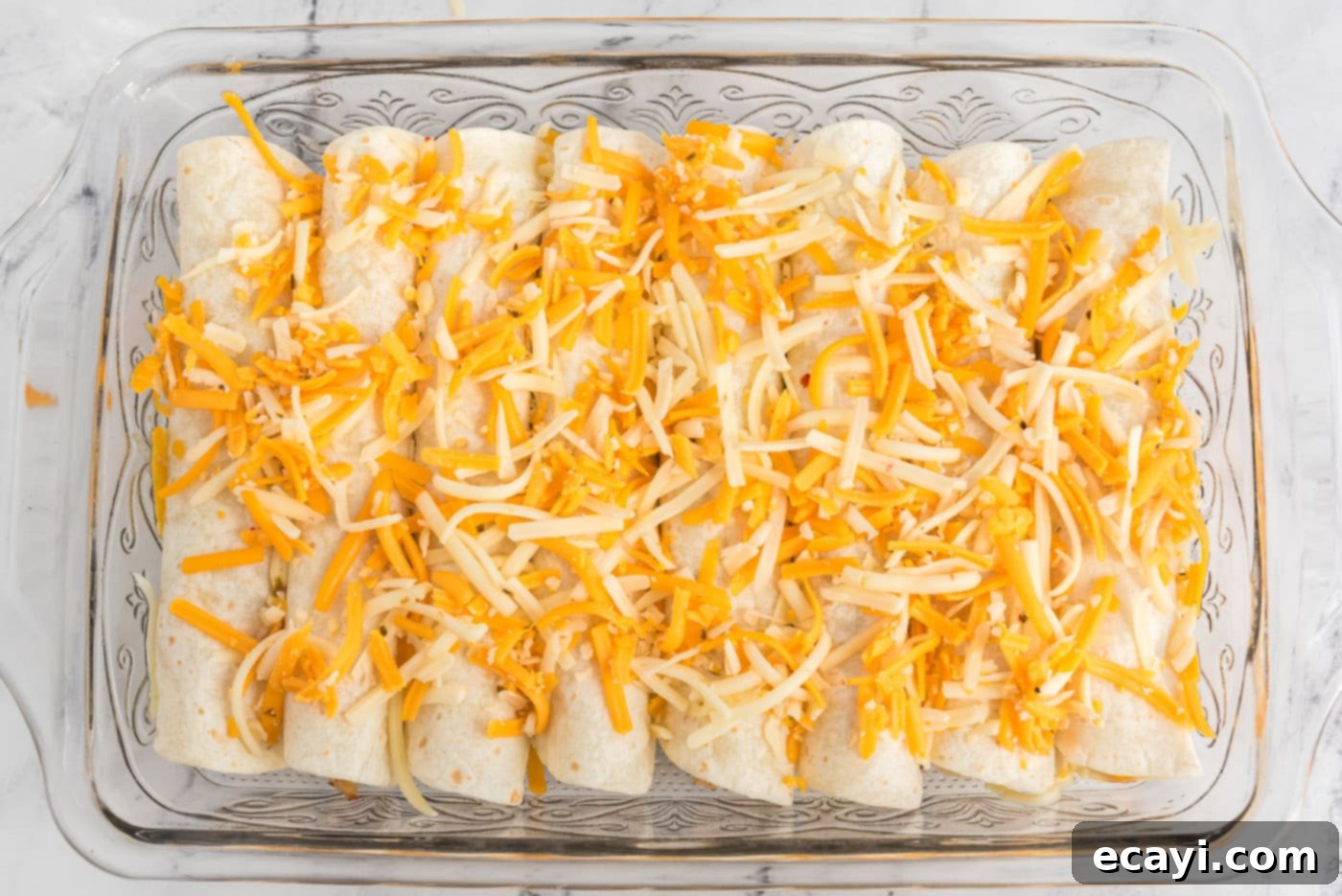 Zesty Chicken Chile Enchiladas 17 Enchiladas generously topped with shredded cheese, ready for the final bake to achieve a golden, bubbly finish.