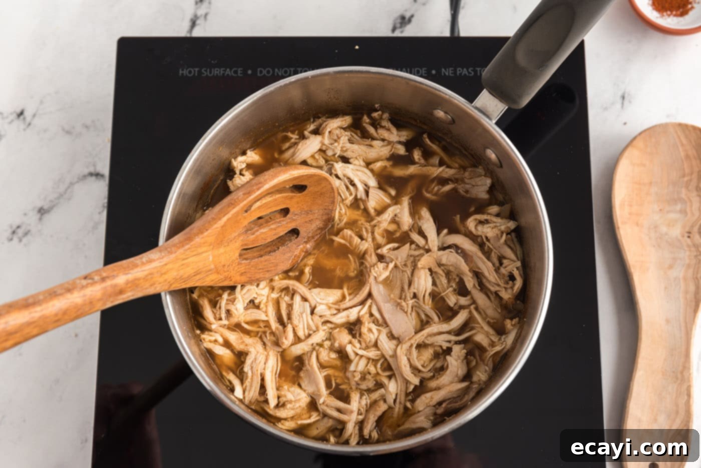 Zesty Chicken Chile Enchiladas 8 Shredded chicken being added to the spiced broth mixture in a pot, ready to simmer and absorb flavors.
