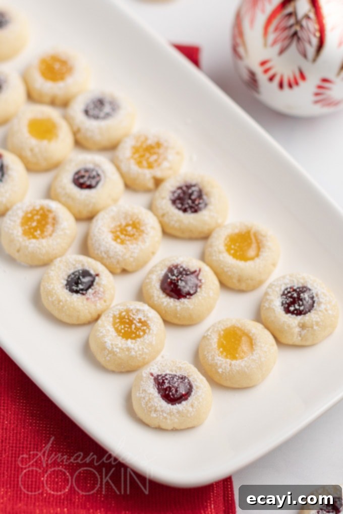 Delicious thumbprint cookies, a perfect soft yet firm treat with a fruity jam-filled center, ideal for festive occasions A baking tray showcasing rows of golden brown thumbprint cookies with various jam fillings, cooling after baking