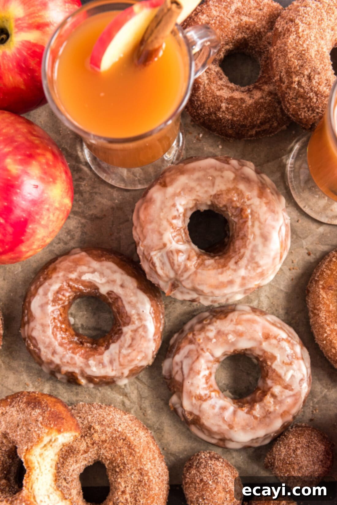 Apple Cider Doughnuts 3 Overhead photo of golden-brown Apple Cider Doughnuts arranged with fresh apples and a jug of apple cider in the background, highlighting the fall theme.