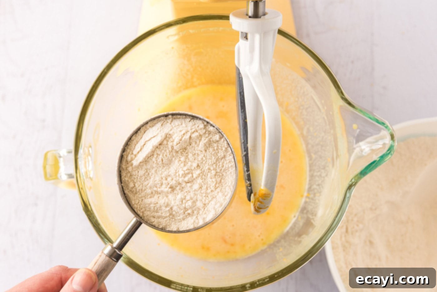 Orange Dream Swirl Cupcakes 7 A cup of flour being gently added over a bowl of orange cupcake batter.