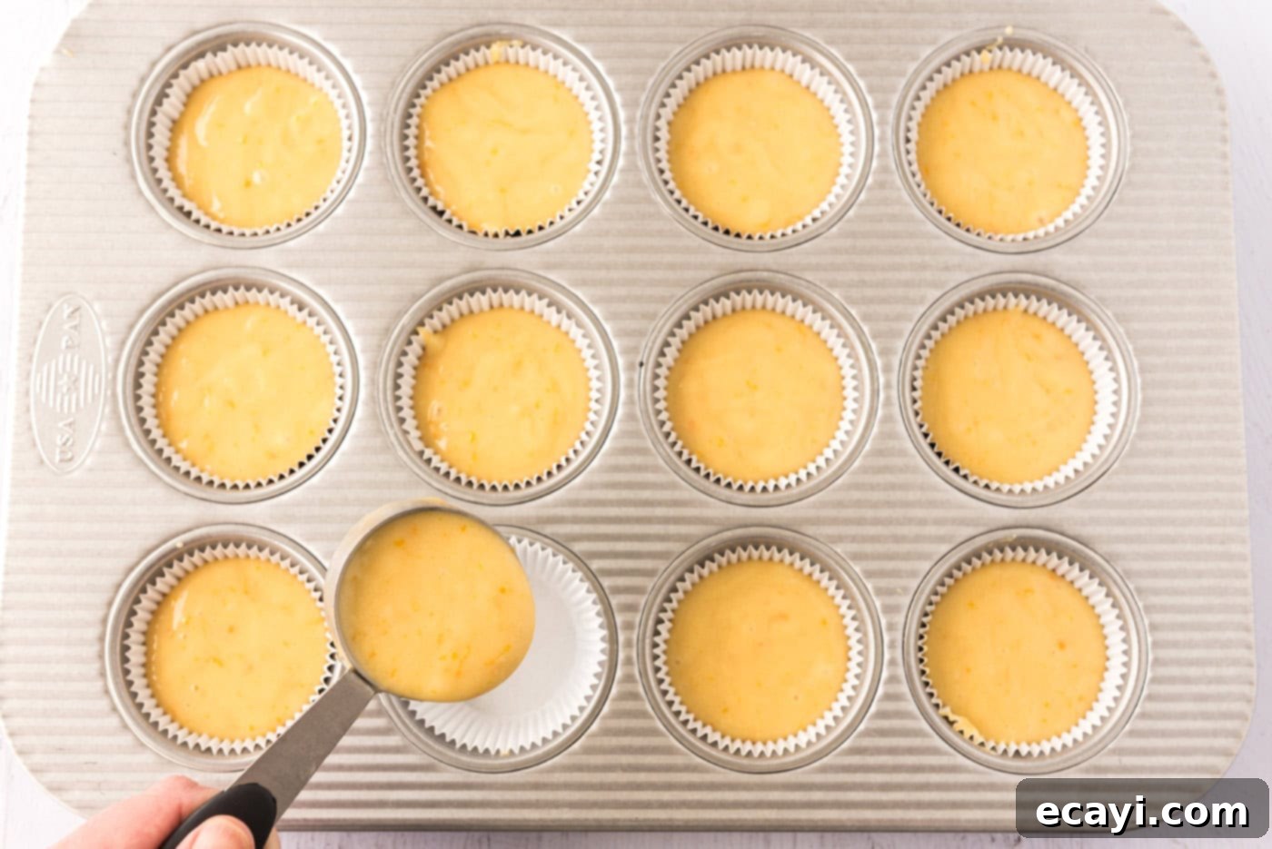 Orange Dream Swirl Cupcakes 9 Cupcake batter being spooned into a muffin pan lined with paper cups.