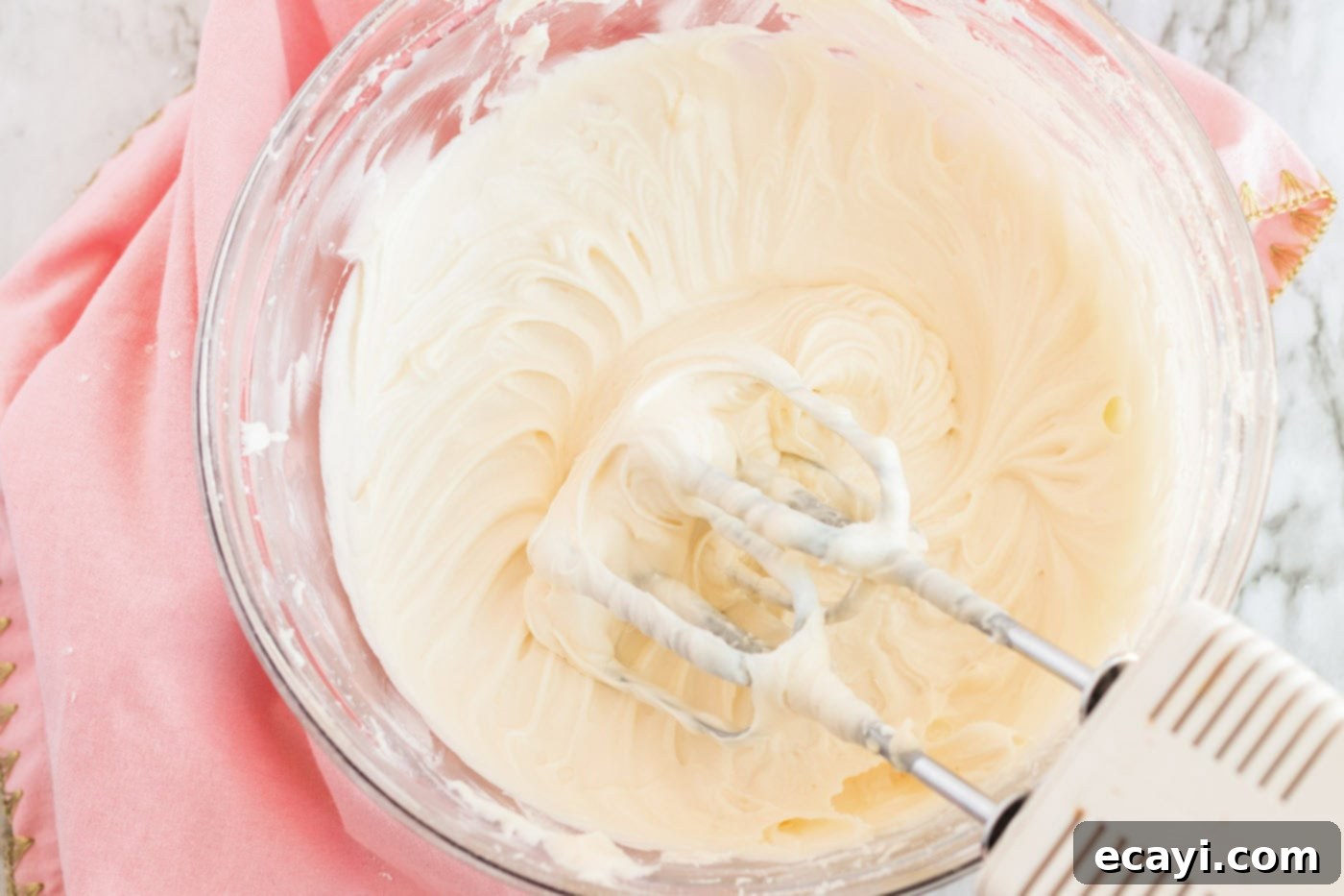 Irresistible Frosted Sugar Cookie Bars 9 Smooth, white frosting in a mixing bowl with a hand mixer resting on the side, ready for coloring.