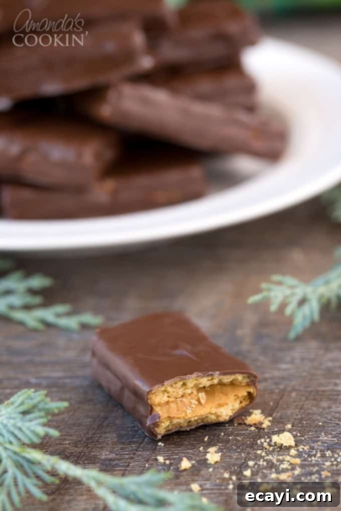 Peanut butter and chocolate lovers and going to go crazy for these super easy to make homemade candy bars. Great for snack or gift giving! #chocolate #candy #desserts #homemade #homemadecandy #candybars #nobake #peanutbutter #valentinesday #peanutbutterdesserts Homemade candy bars cut in half, showing distinct layers of graham cracker, creamy peanut butter, and a smooth chocolate coating