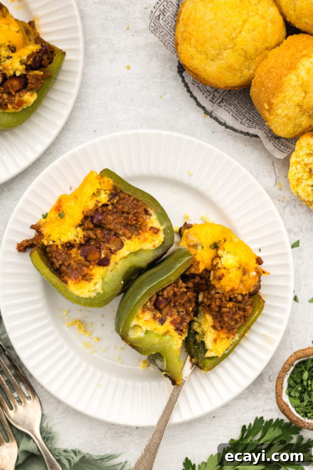 Chili Cornbread Stuffed Peppers 2 A chili and cornbread stuffed bell pepper cut in half, revealing the layers of chili and cornbread, on a plate, garnished with fresh herbs.