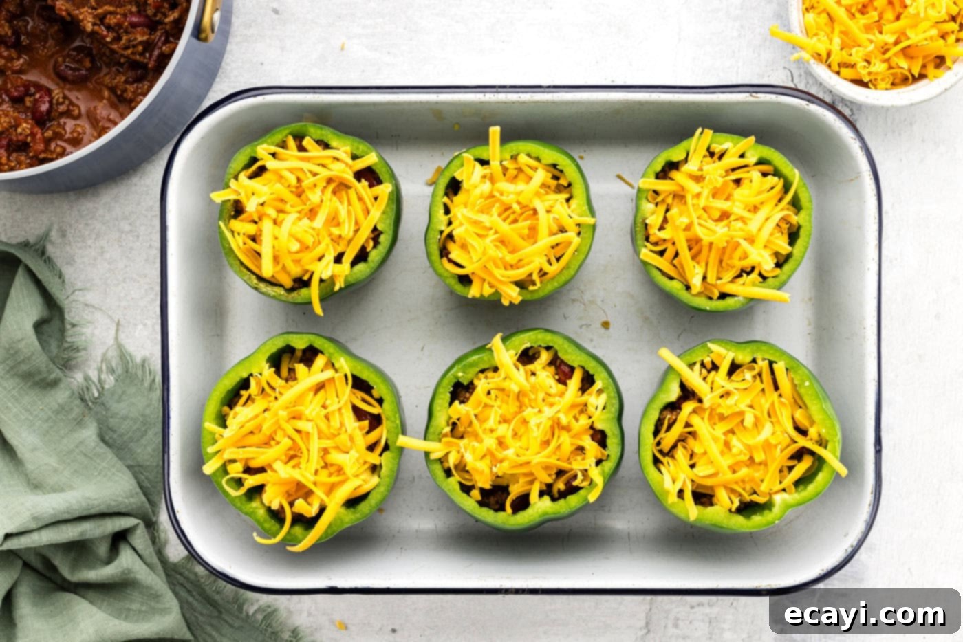 Chili Cornbread Stuffed Peppers 11 Shredded cheddar cheese generously sprinkled over chili and cornbread stuffed bell peppers, ready for baking.