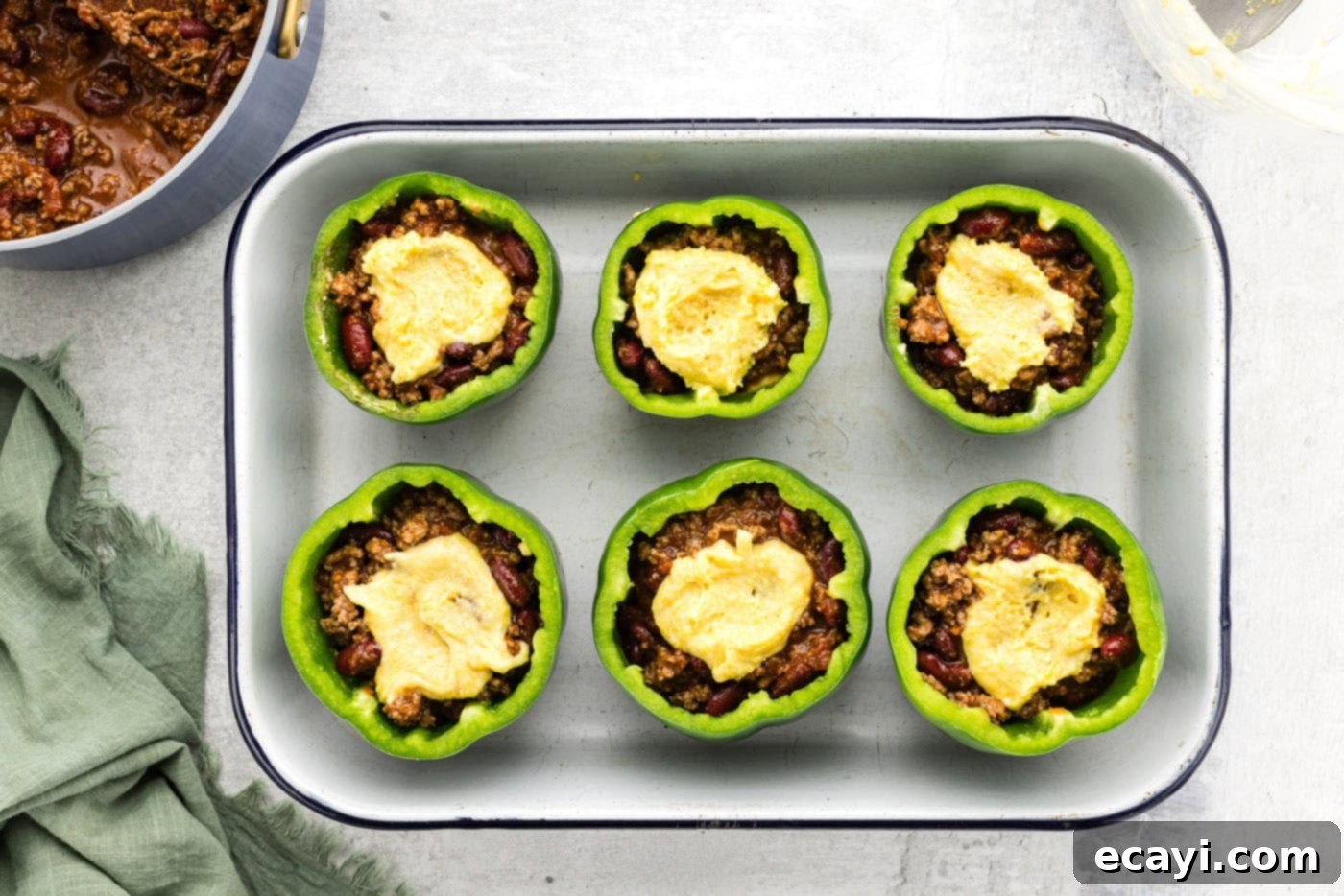 Chili Cornbread Stuffed Peppers 10 Cornbread batter being spooned on top of chili-filled bell peppers in a baking dish, creating a top layer.