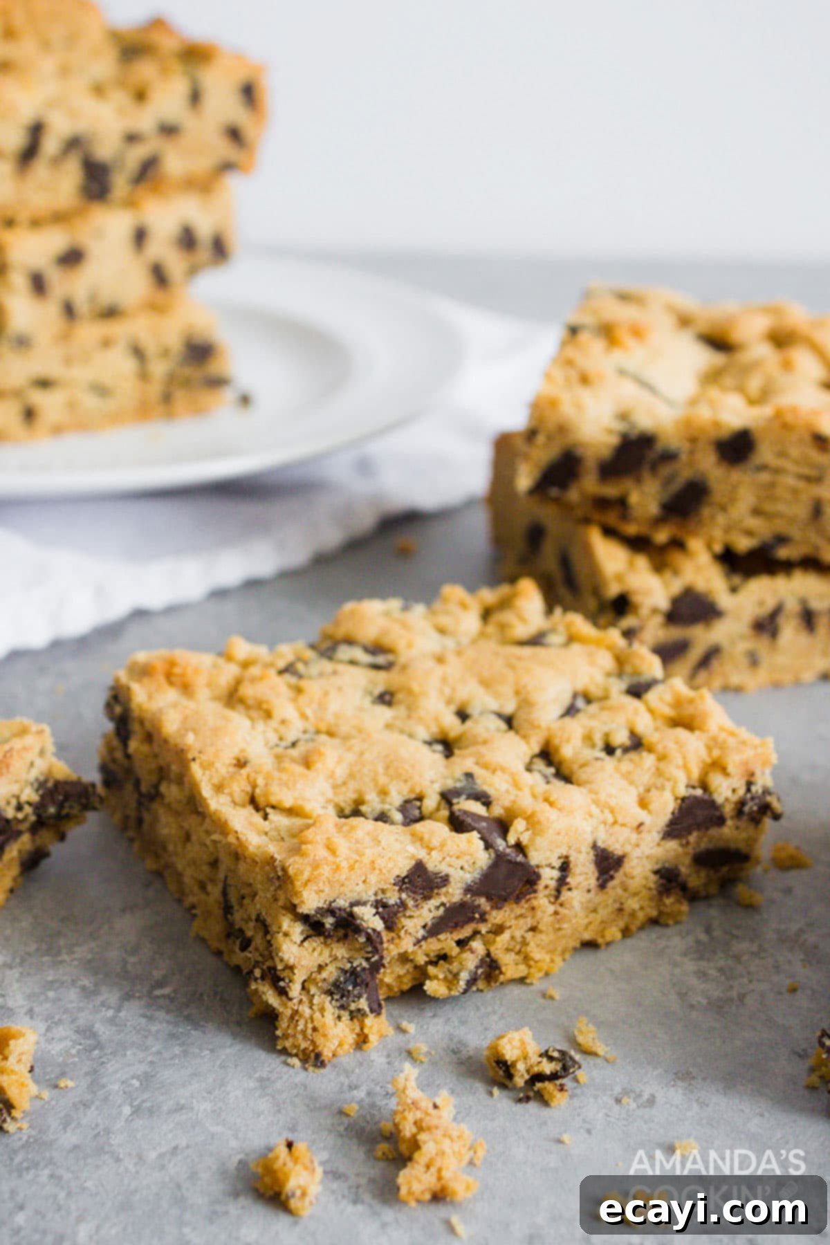 Ultimate Peanut Butter Chocolate Chip Bars 4 A single chewy peanut butter chocolate chip bar prominently displayed on a kitchen counter, with a blurred background of more bars in the baking pan.