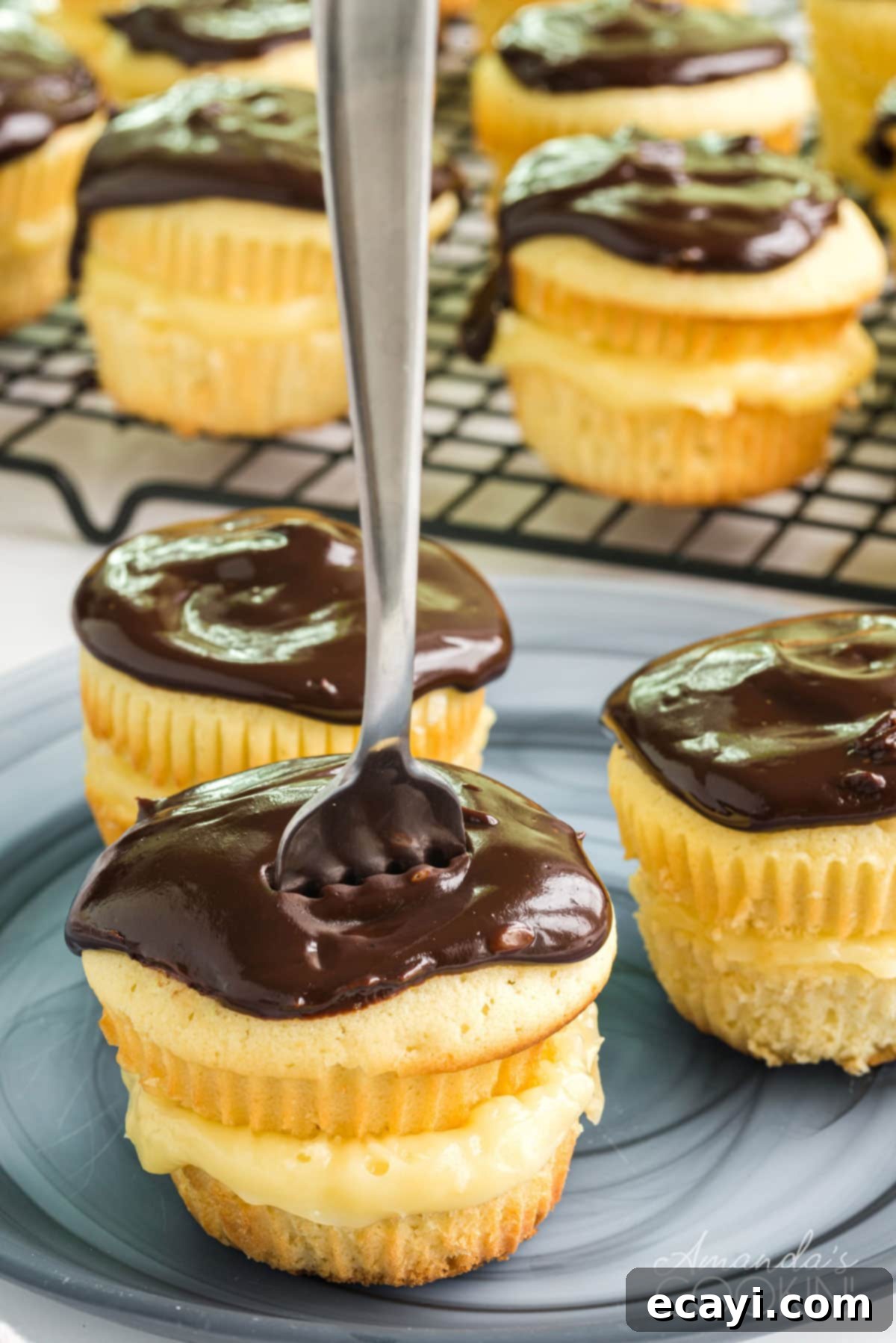 Inside a Boston Cream Cupcake: Vanilla Cream and Ganache A sliced Boston Cream Cupcake with a fork revealing the creamy vanilla filling and chocolate topping