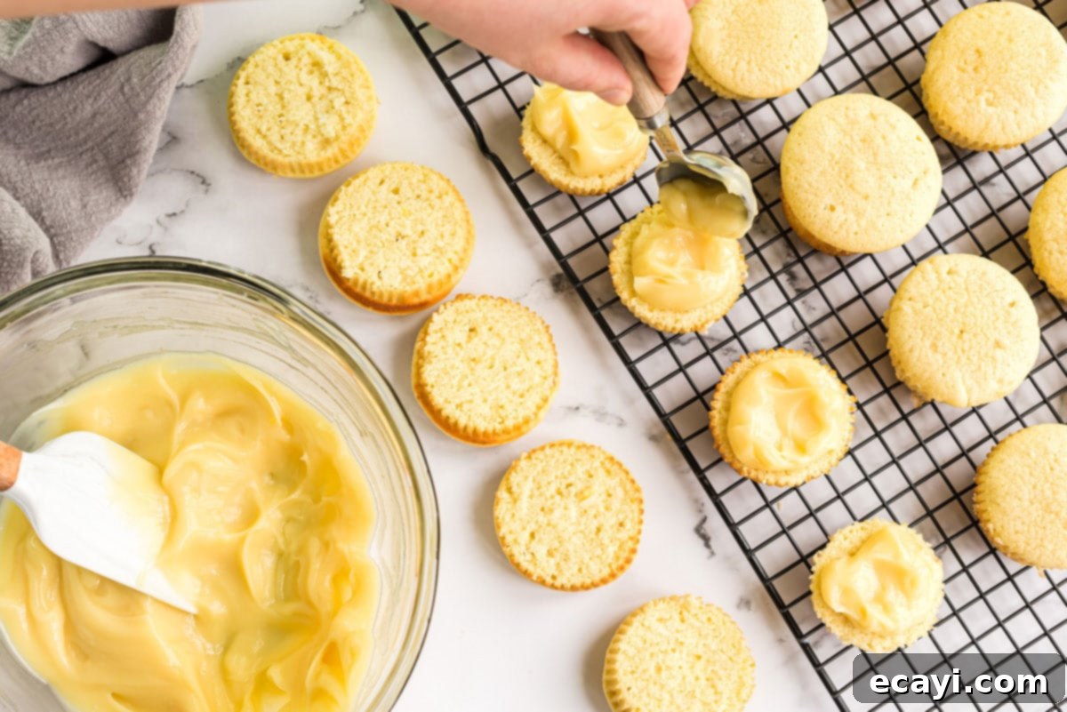 Filling a Boston Cream Cupcake with Vanilla Cream Spoonful of vanilla pudding filling being spread onto a sliced cupcake