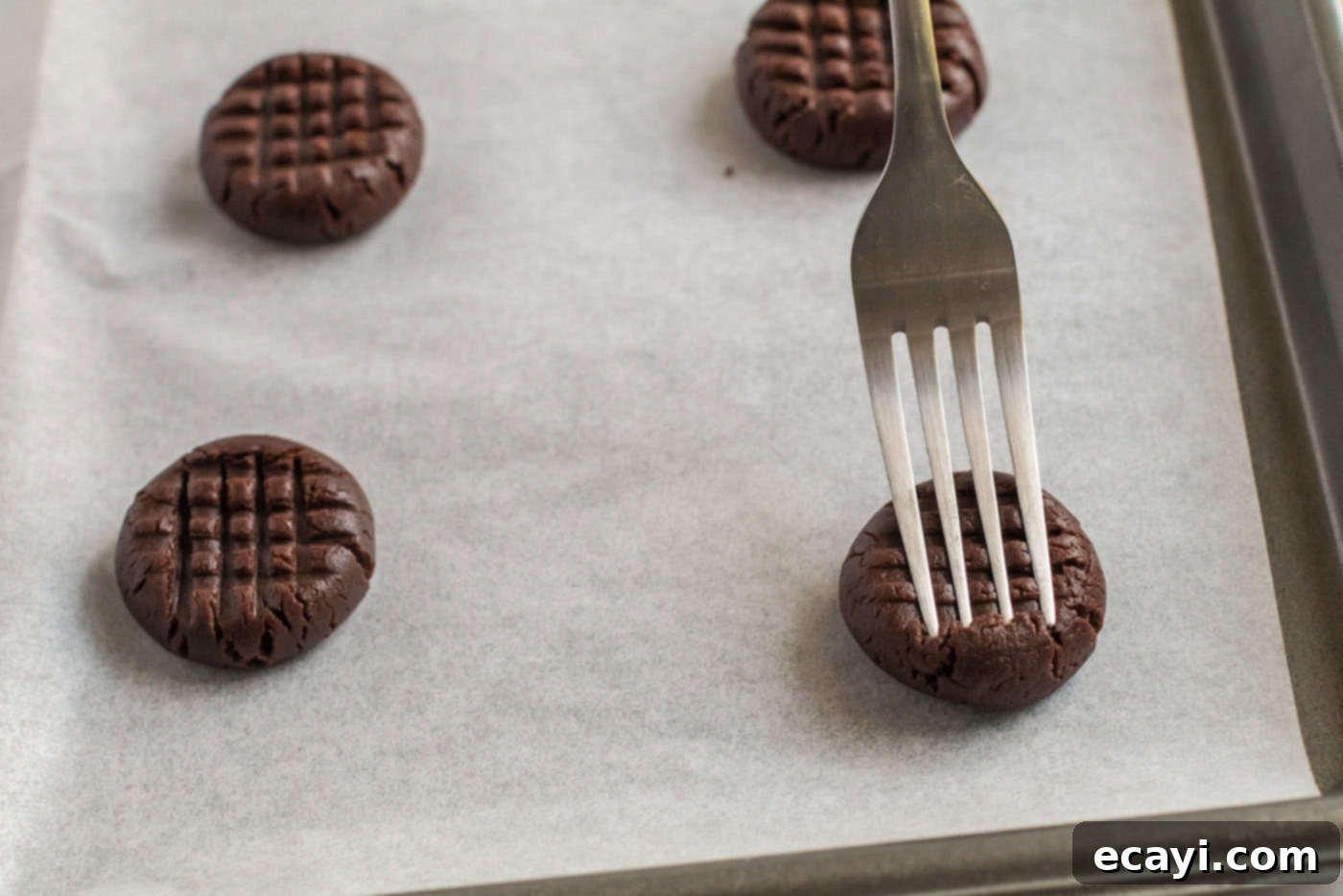 The Ultimate Chocolate Peanut Butter Cookies 8 A fork gently pressing down on a chocolate peanut butter cookie dough ball, forming the classic crisscross pattern.