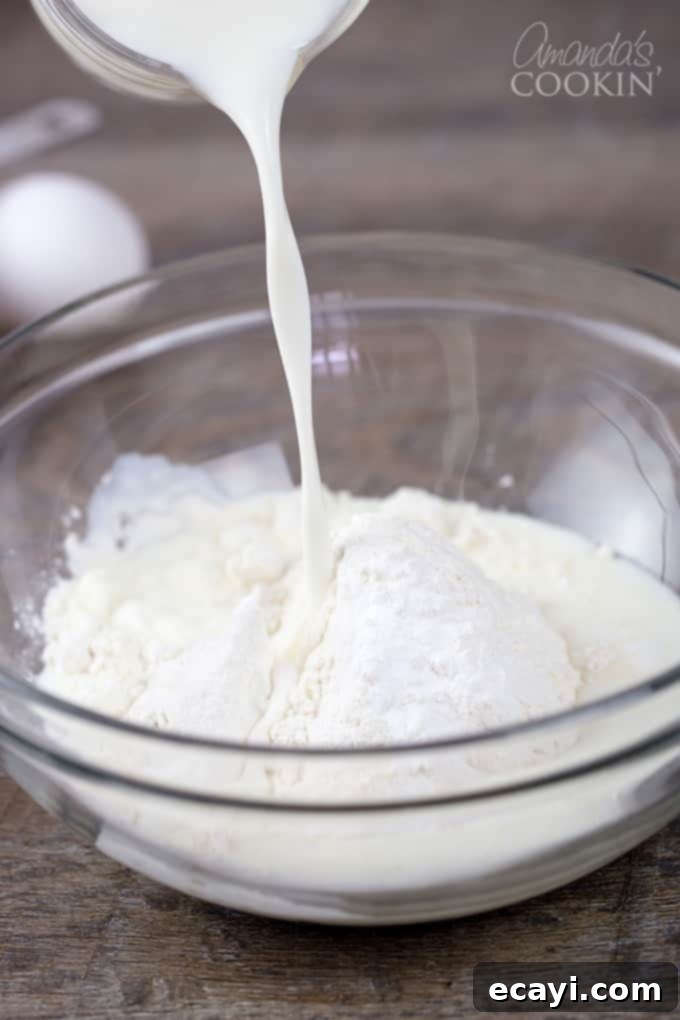 Cheesy Pepperoni Pizza Bites 5 A clear glass bowl containing flour with milk being poured in, illustrating the initial mixing step for the pizza puff batter.