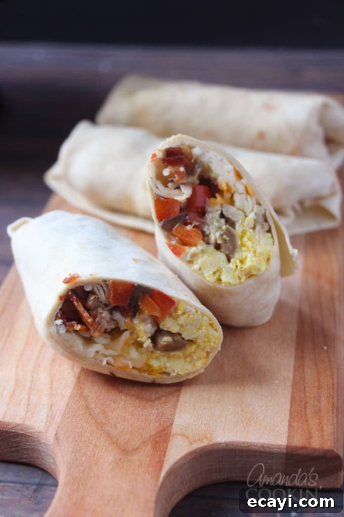 Sunrise Burritos 3 Two halves of a breakfast burrito stacked on top of each other, with several whole burritos in the background, all on a wooden cutting board.