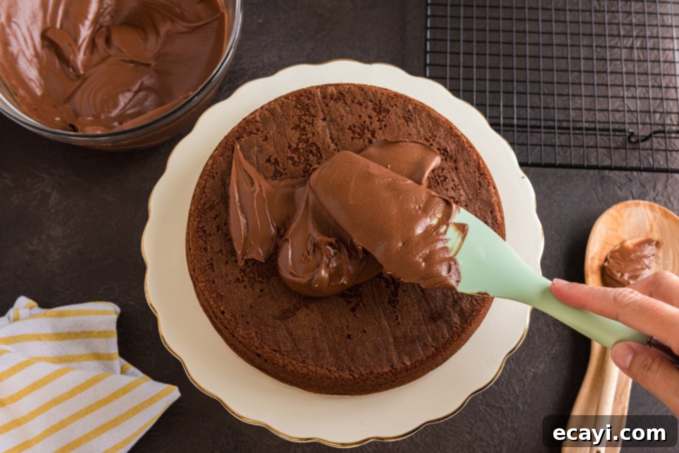 Decadent Chocolate Fudge Delight 23 spreading chocolate fudge frosting over chocolate cake with a rubber spatula