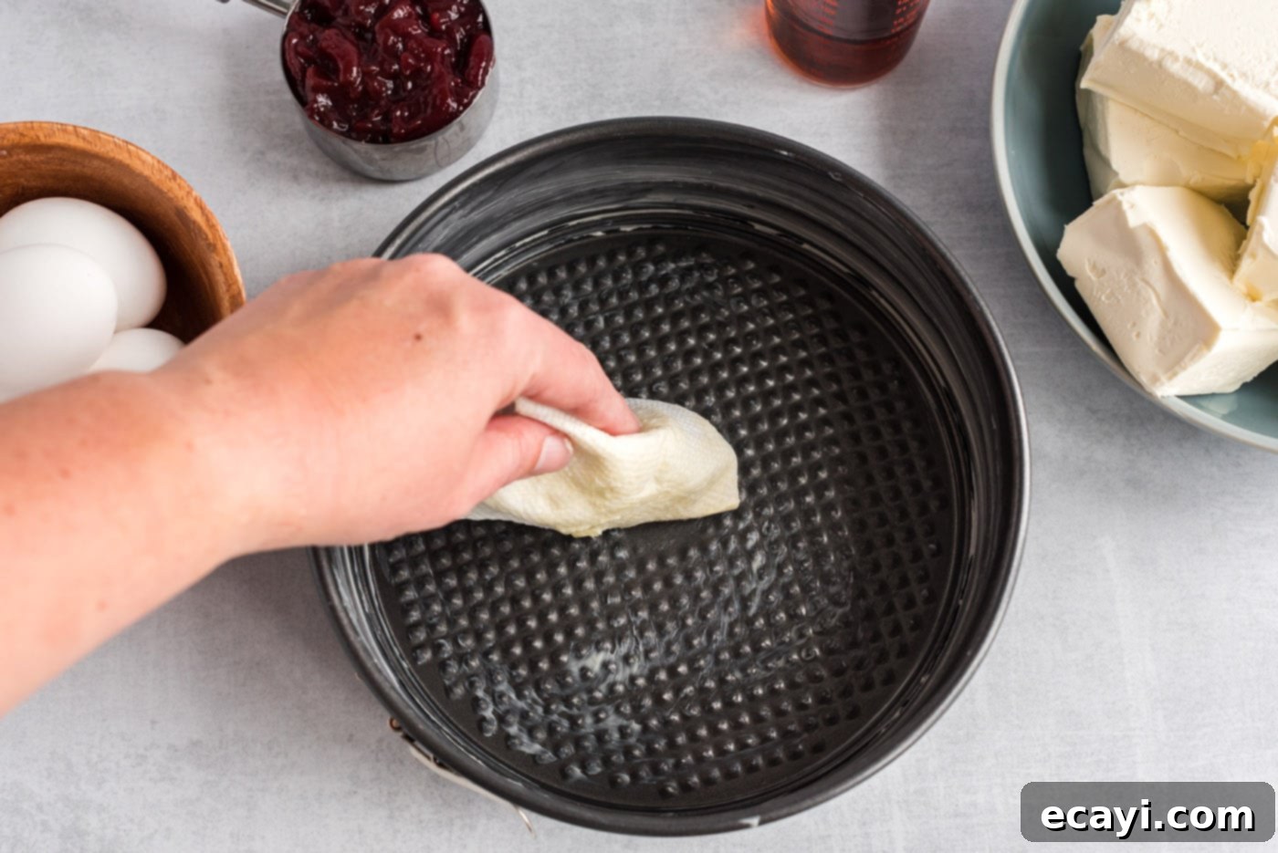 Regal Trifle Cheesecake 5 A hand buttering the bottom and sides of a 9-inch springform pan, preparing it for the cheesecake.
