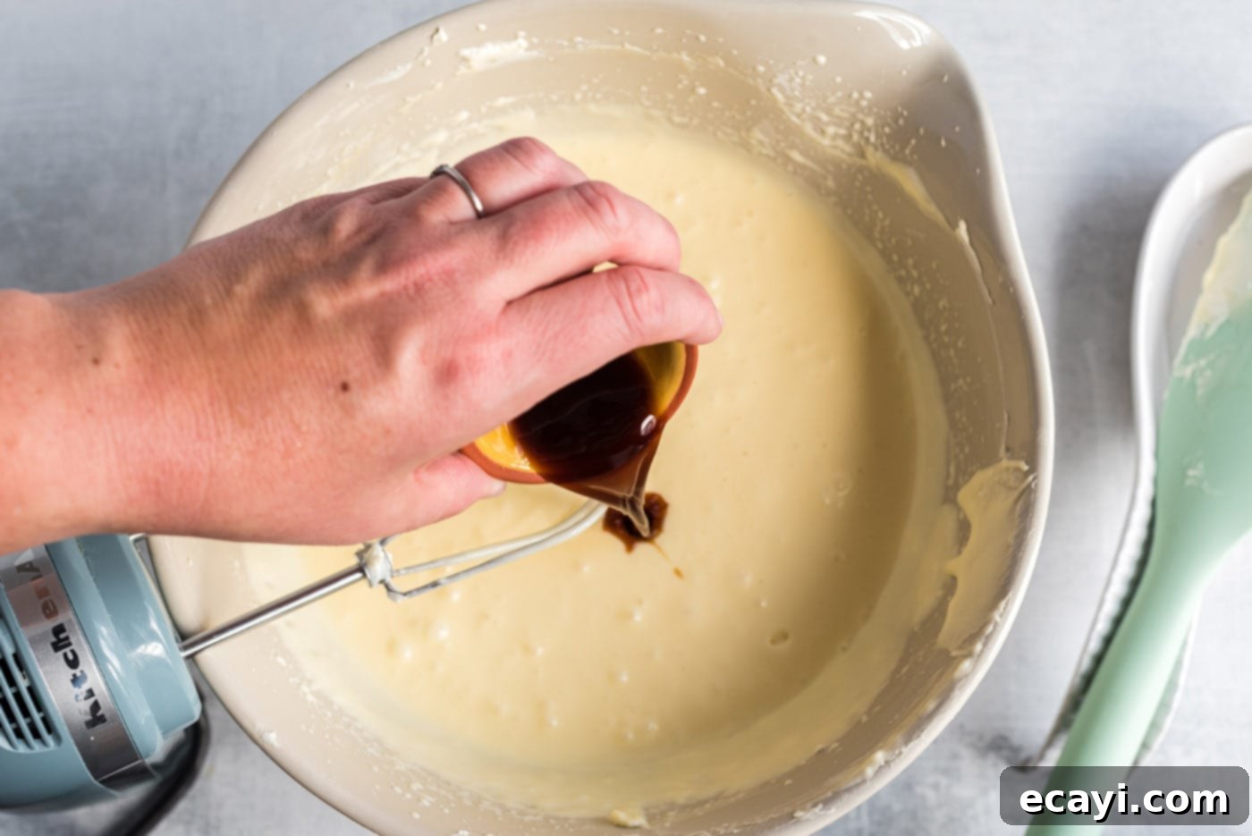 Regal Trifle Cheesecake 8 Vanilla extract being poured into a bowl of creamy cheesecake mixture, mid-preparation.