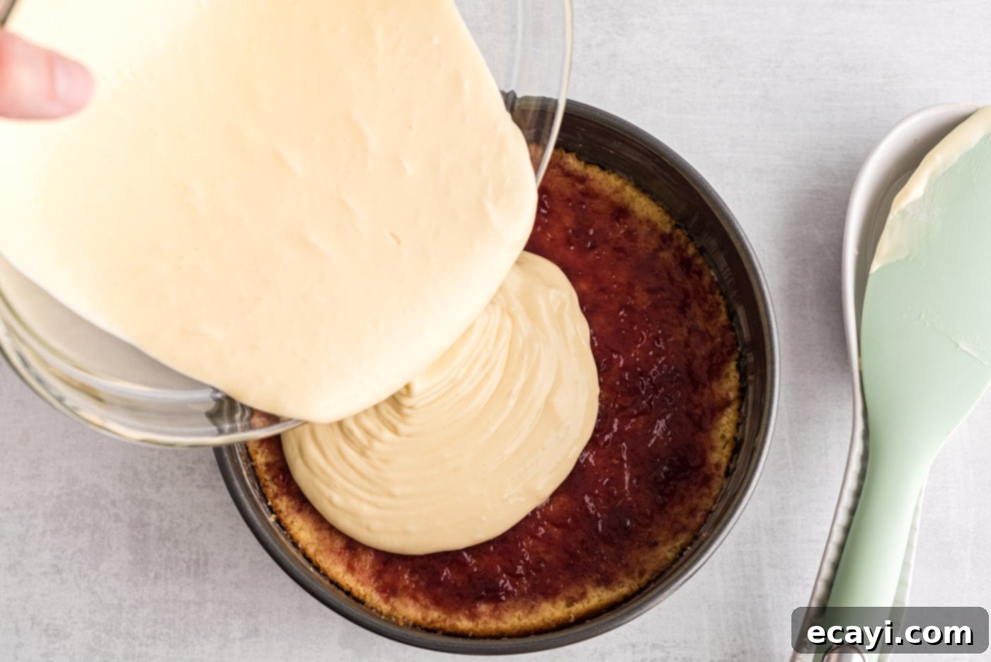 Regal Trifle Cheesecake 9 Thick, creamy cheesecake batter being poured over the raspberry preserves and cake layer in a springform pan.