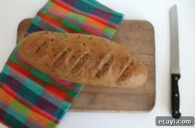 Garden Fresh Garlic & Herb Bread 2 A whole loaf of scallion chive bread with garlic and rosemary resting on a wooden cutting board, showcasing its golden crust.