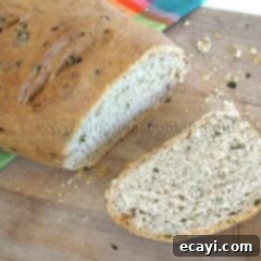 Garden Fresh Garlic & Herb Bread 3 A close up photo of a sliced loaf of scallion chive bread with garlic and rosemary on a wooden cutting board.
