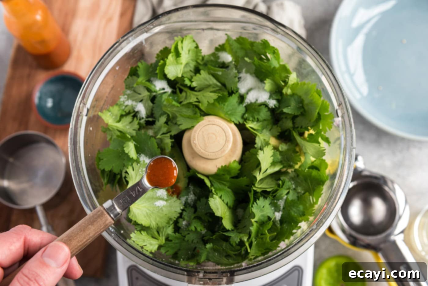 Vibrant Tomatillo Avocado Onion Salsa 7 adding hot pepper sauce to food processor with cilantro, onion, avocado, and chile peppers, showing final ingredients before blending