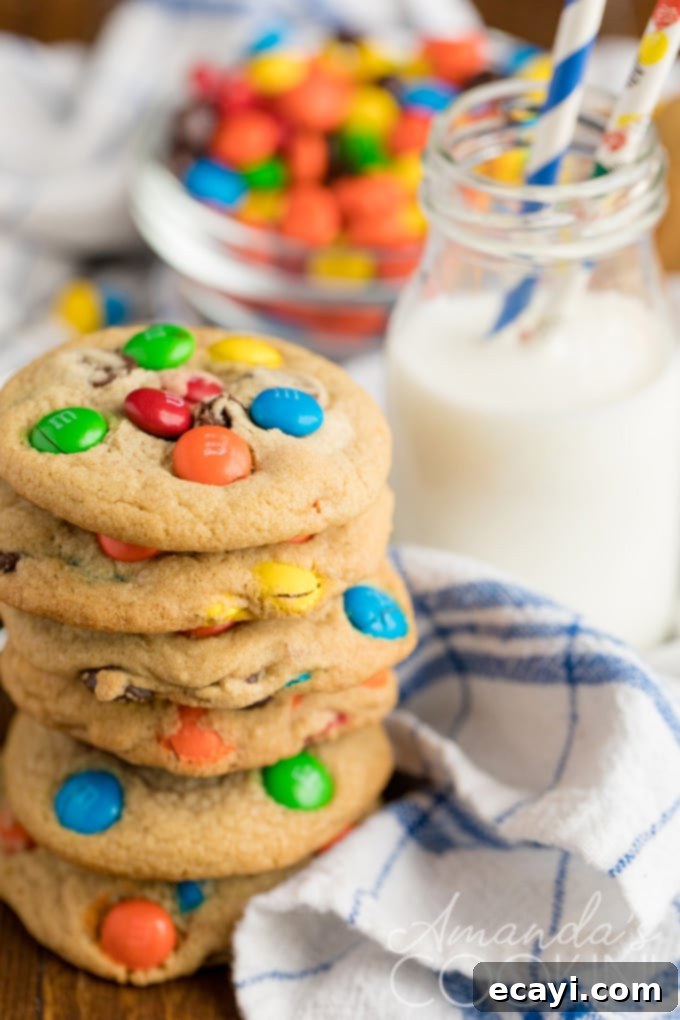 Jumbo Chocolate Chip M&M Cookies are easy to make, full of chocolate chips and M&M candies, and loved by all. Freshly baked jumbo M&M chocolate chip cookies with a glass of milk on a white surface.
