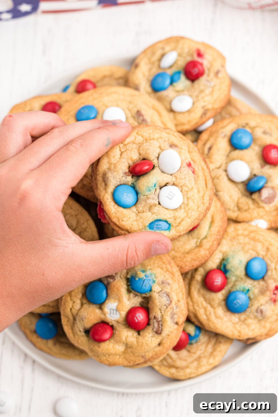 Colorful M&M Chocolate Chip Cookies 2 A child's hand reaching for a patriotic red, white, and blue M&M cookie from a white plate