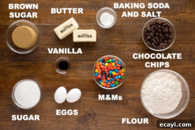 All the ingredients you need for delicious, jumbo Chocolate Chip M&M Cookies are ready for baking. A collection of measured ingredients for chocolate chip M&M cookies laid out on a wooden surface, including butter, sugars, eggs, flour, chocolate chips, and M&M candies.