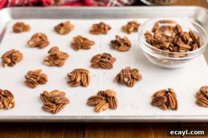 Pecan mounds on a baking sheet, forming the base for homemade chocolate turtles. Small mounds of toasted pecans arranged on a baking sheet, ready for caramel